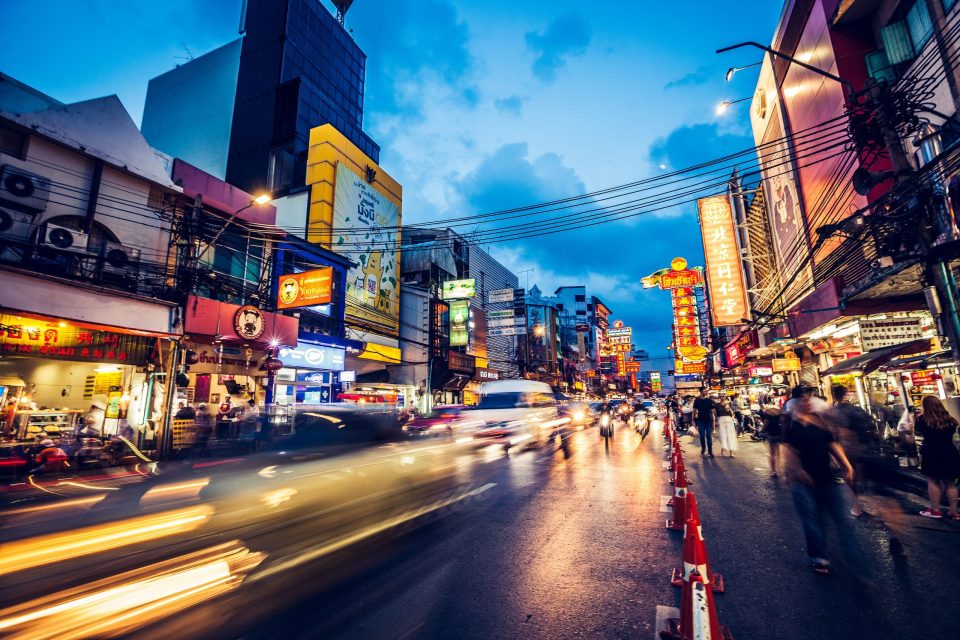 A commercial urban street at dusk is illuminated by numerous signs in Asian script.
