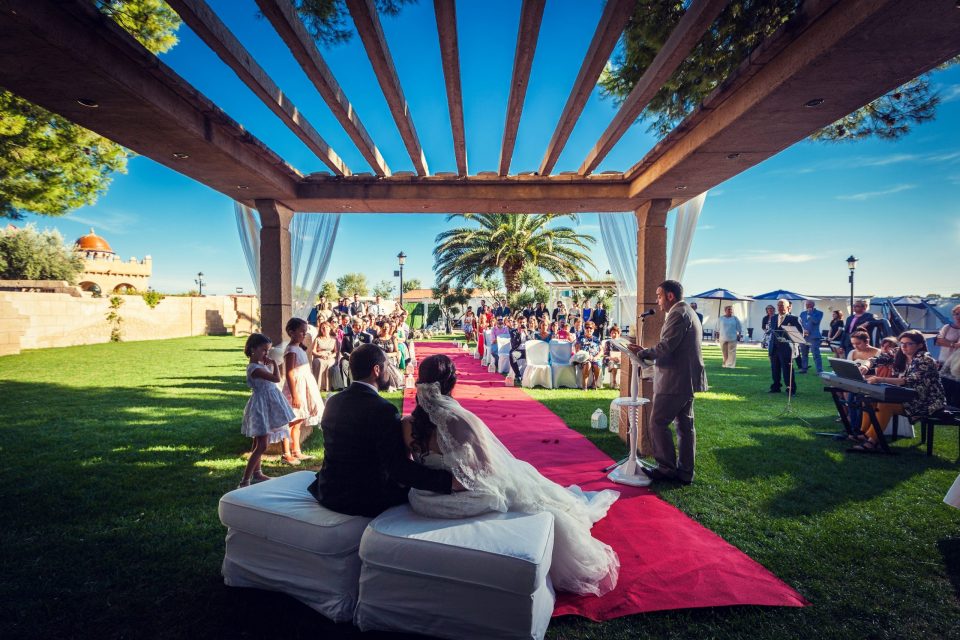 Ceremonia de boda al aire libre en una finca, bajo una pérgola de madera con telas blancas.