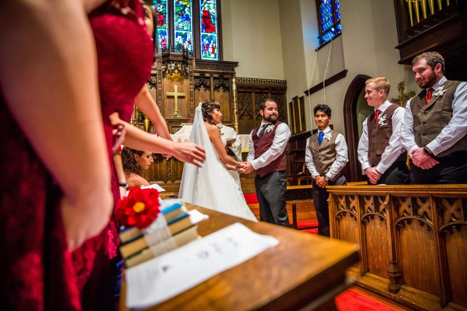 A couple stands in front of the altar during a wedding ceremony as several people look on.