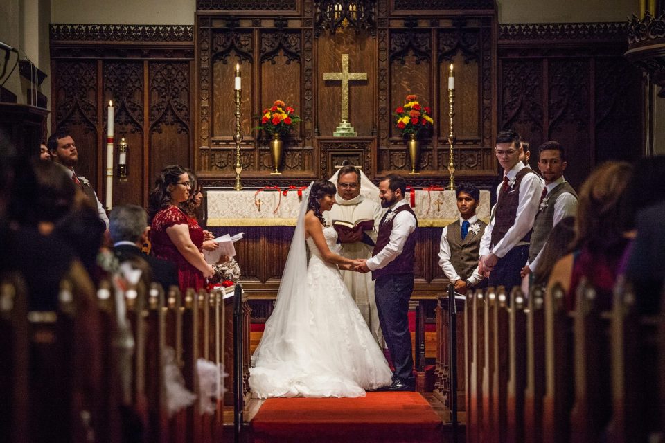 The bride and groom hold hands in front of the altar during a wedding ceremony inside a church.
