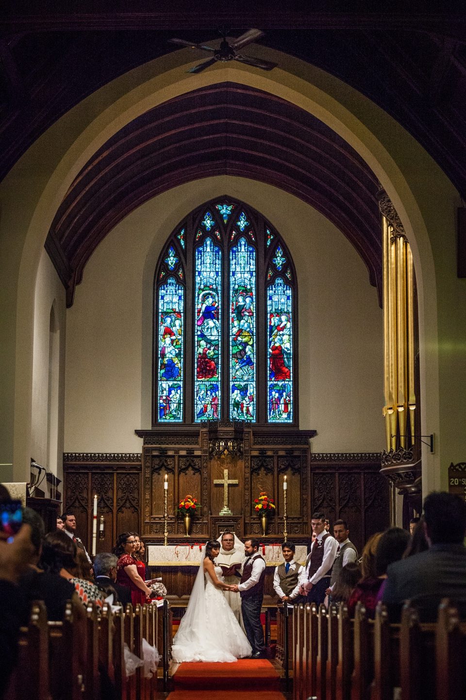 A wedding ceremony is taking place inside a church, with a couple beside the altar.