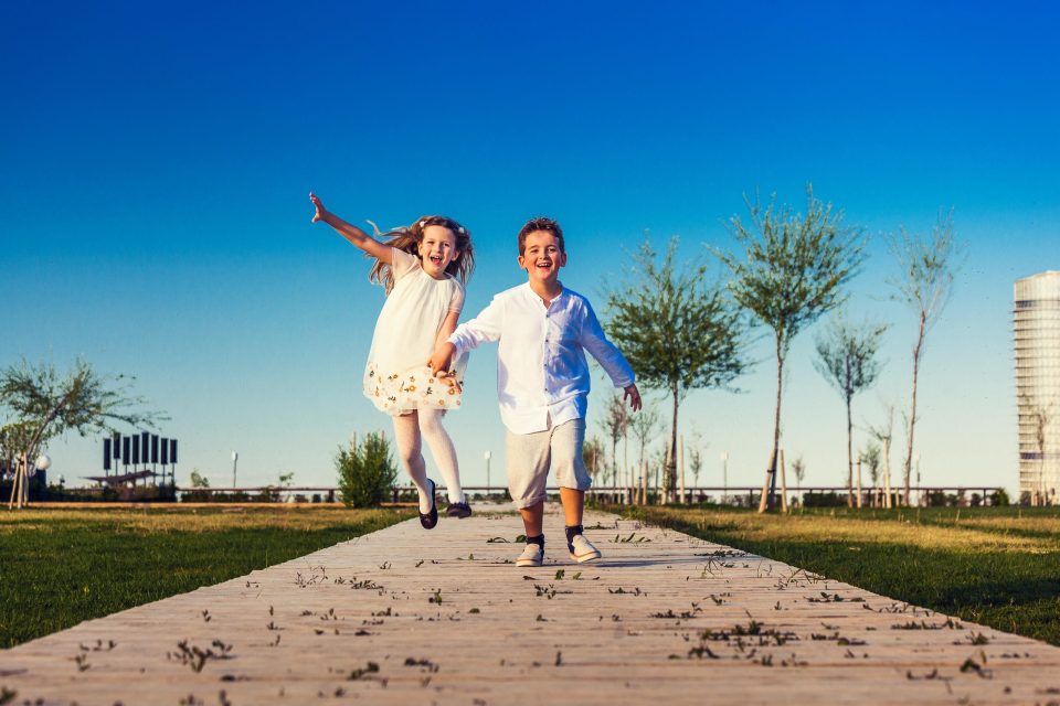 Dos niños corren agarrados de la mano por una pasarela de madera en un parque.