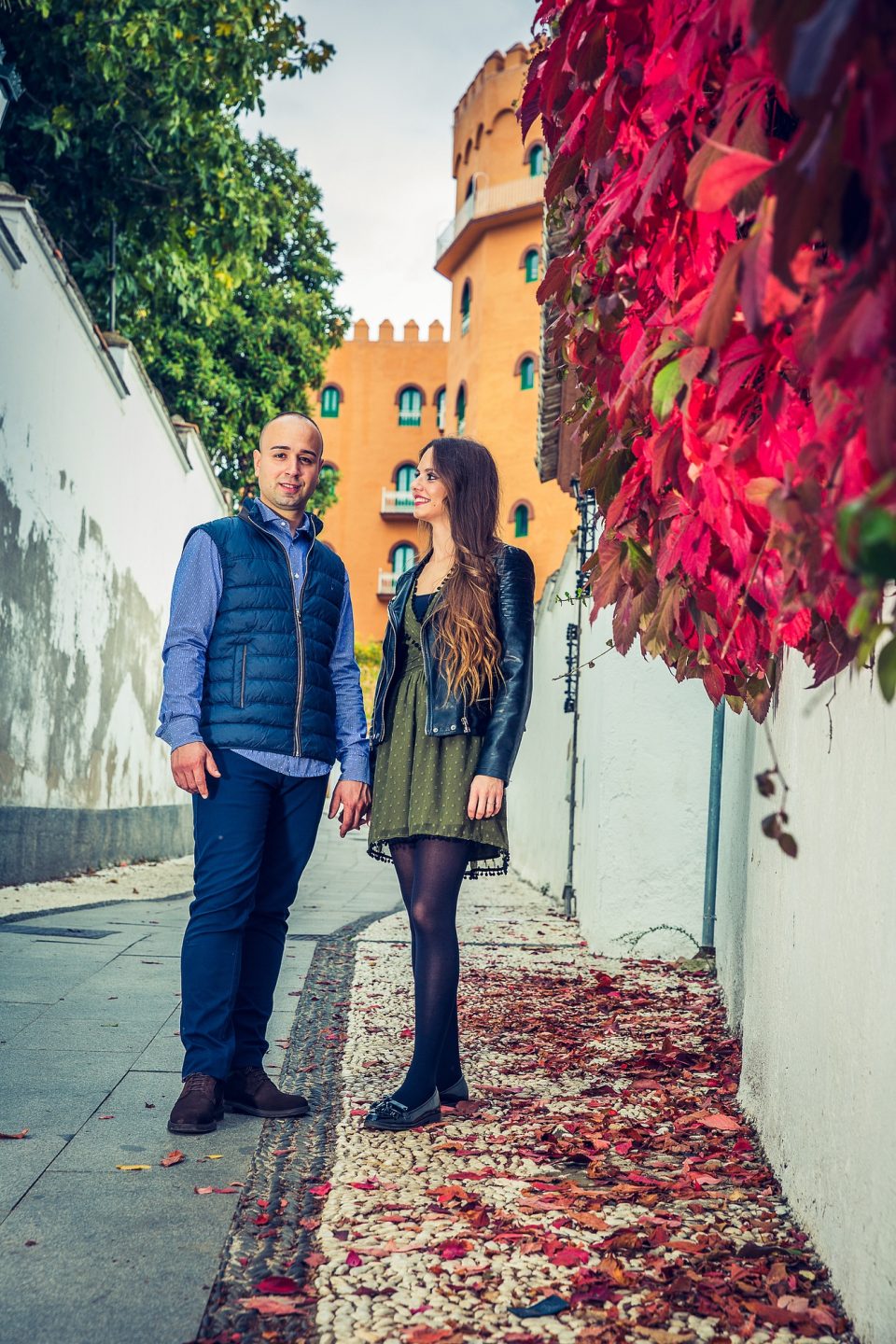 Two people walk along a narrow street between white walls.