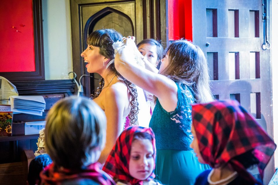 A woman with her hair tied back has a floral adornment fitted during wedding preparations.