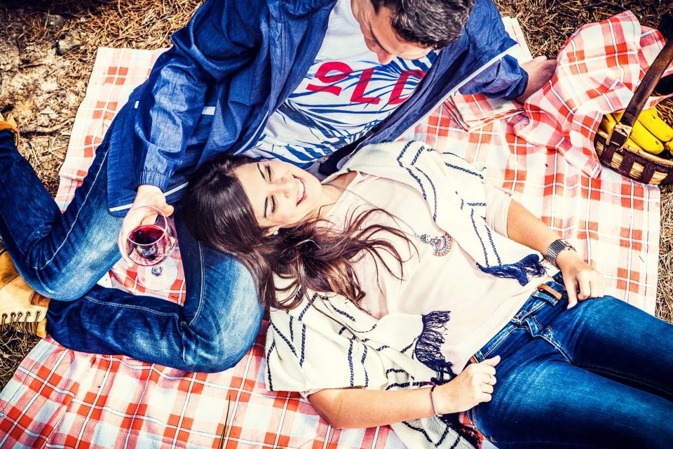 Fotografía cenital de una pareja tumbada sobre una manta de picnic a cuadros rojos y blancos.
