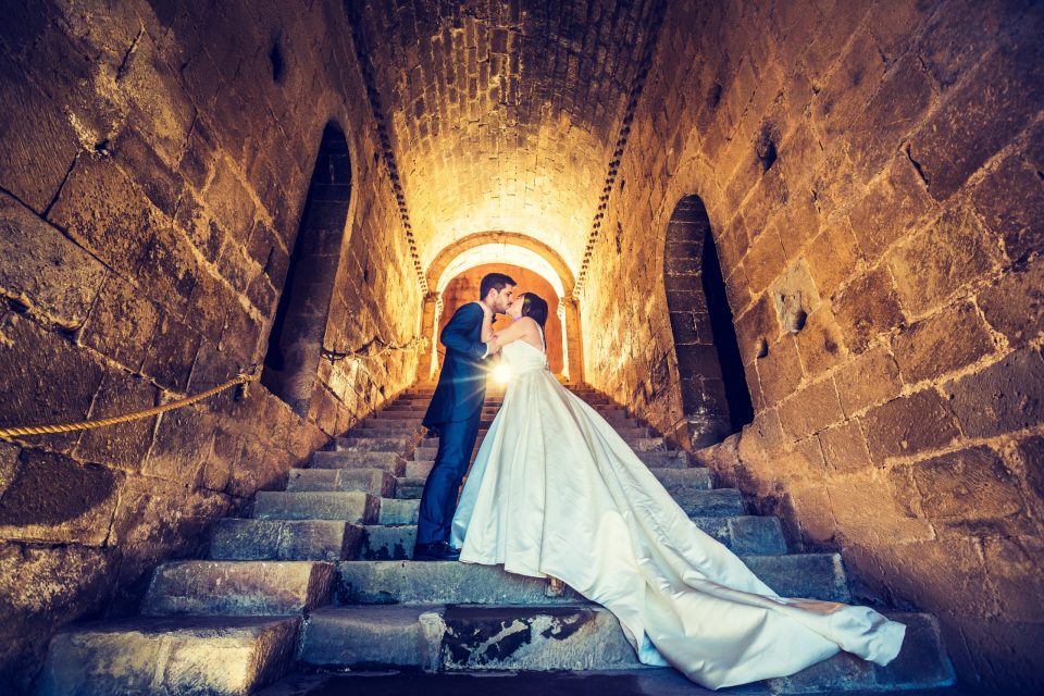 Fotografía de una pareja de novios besándose en una escalera de piedra dentro de una iglesia.
