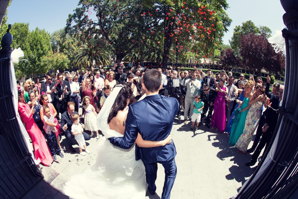 Fotografía de una pareja de novios saliendo de una iglesia mientras sus familiares y amigos los reciben entre aplausos.
