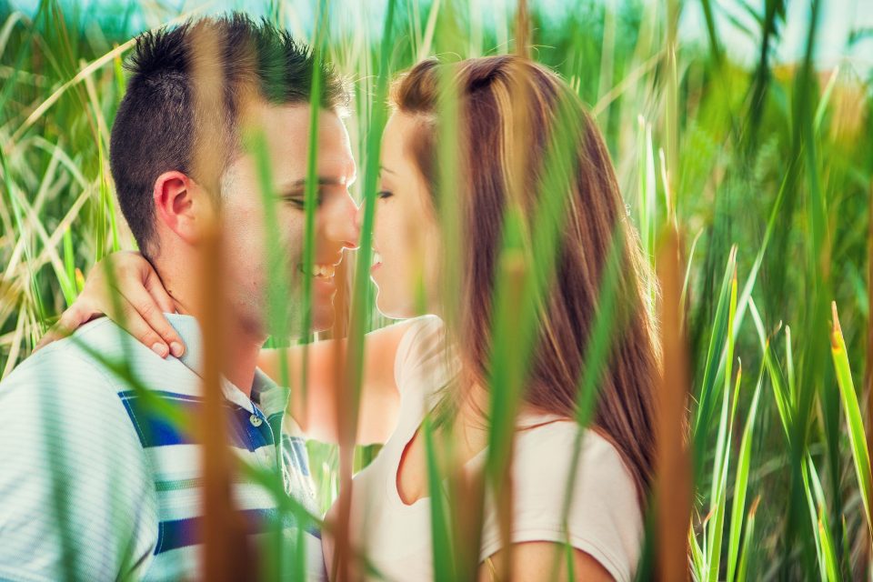 Fotografía de una pareja en un parque, parcialmente oculta entre cañas altas y vegetación verde.