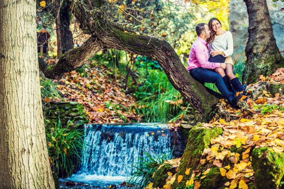 A couple sits on a sloping log in a wooded rural setting.