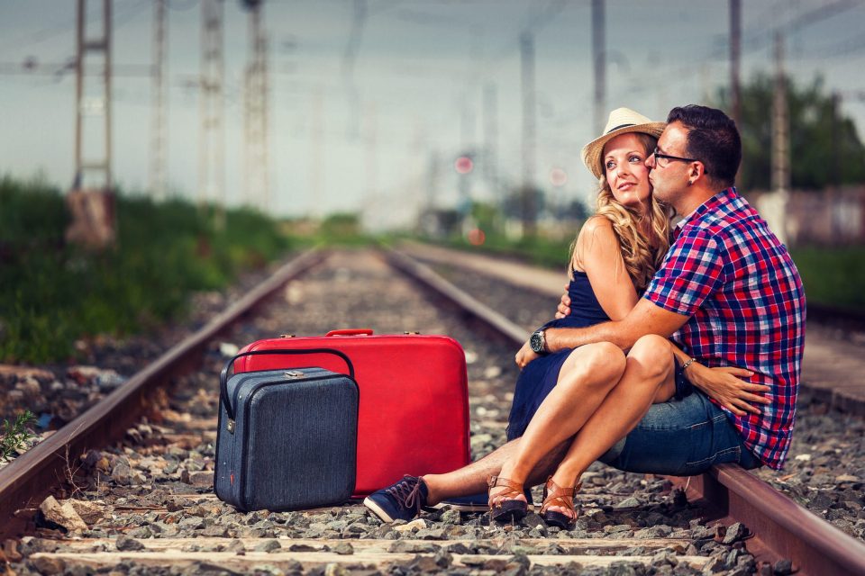 Fotografía de una pareja sentada y abrazada sobre unas vías de tren al aire libre.