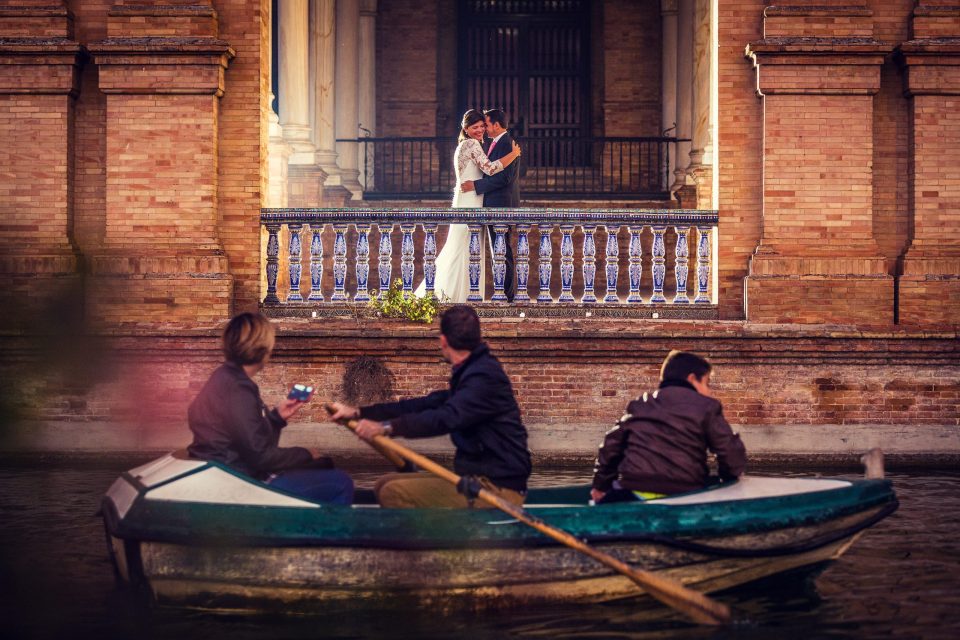 Fotografía de una pareja vestida de boda abrazándose en un balcón decorado con azulejos.