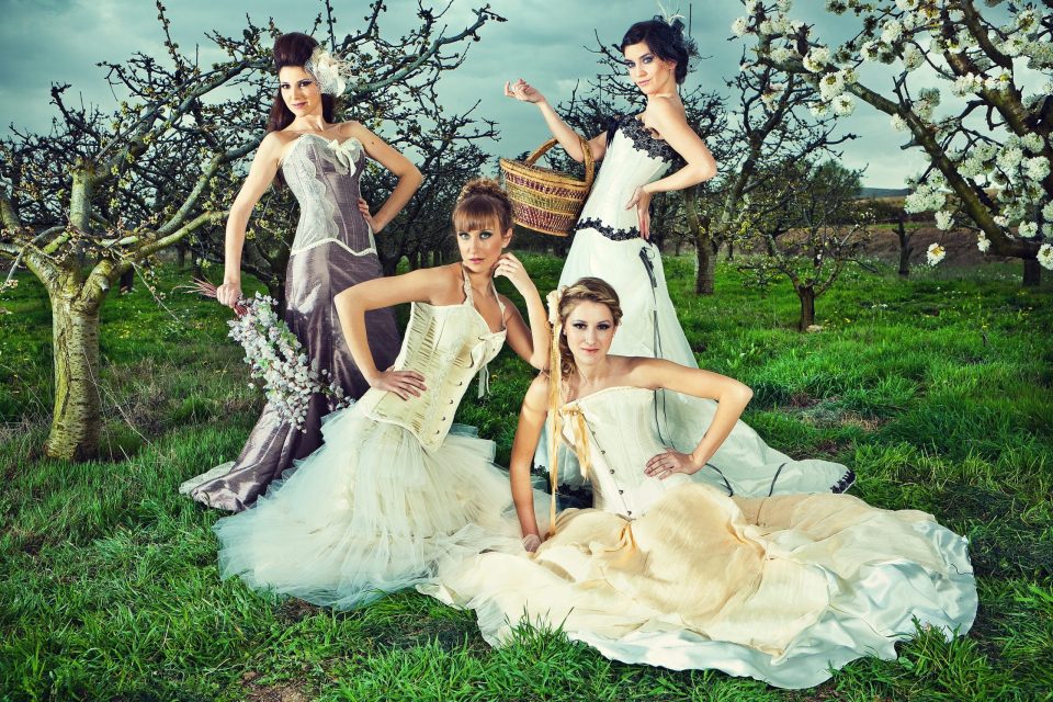 Fotografía editorial de glamour con cuatro modelos posando en un prado dentro de un huerto de árboles frutales en flor.