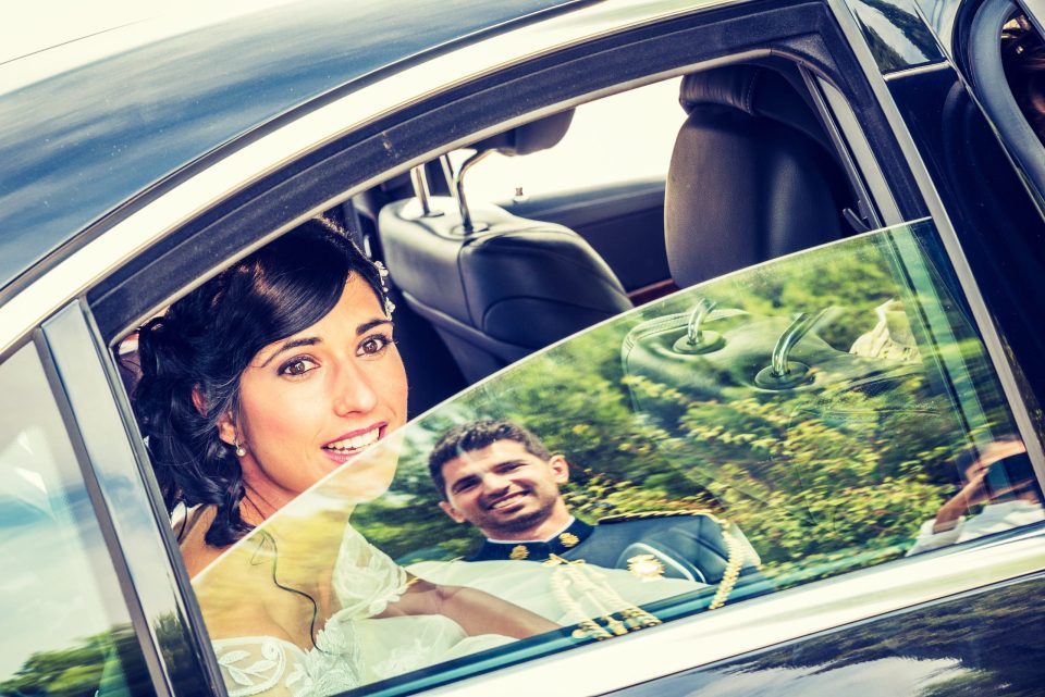 Fotografía en exterior, con luz natural, de una novia sentada dentro de un coche.