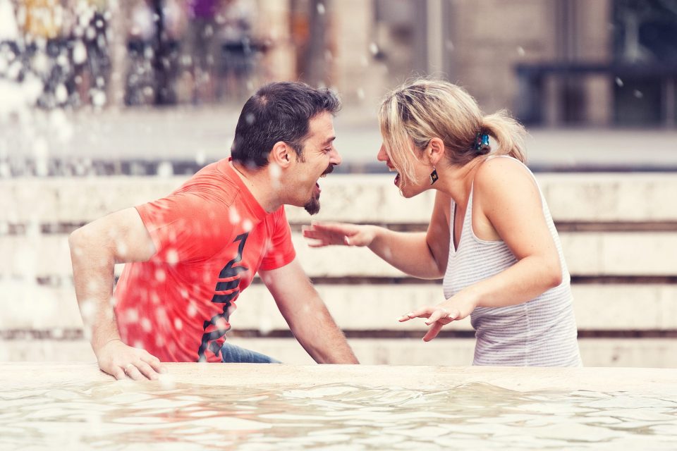 Fotografía espontánea de una pareja riendo y jugando junto a una fuente urbana.