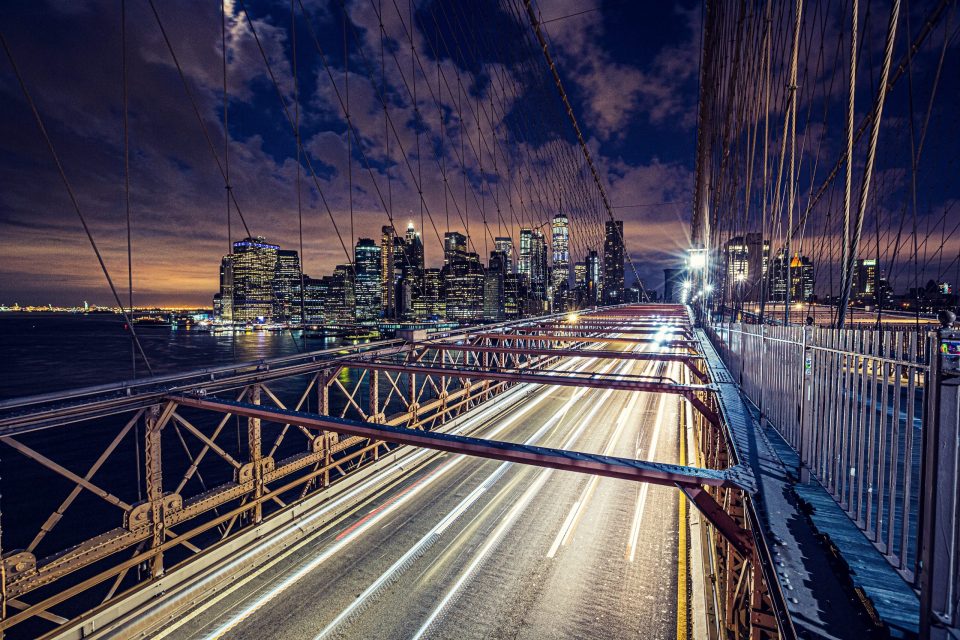 A night-time photograph shows an urban suspension bridge with numerous cables and metal structures in the foreground.