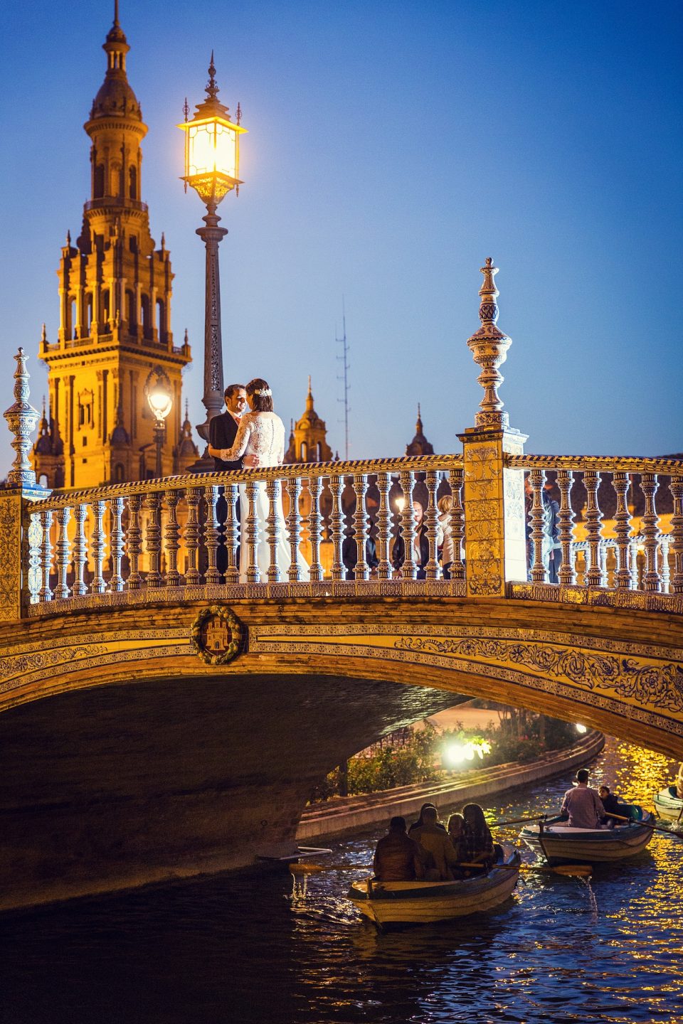A night-time photograph shows an ornate illuminated bridge with a monumental tower and decorative street lamps in the background.