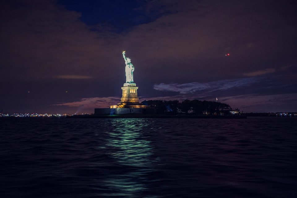 A night-time photograph shows an illuminated monumental statue beside the water.