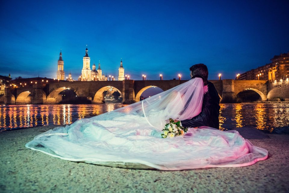 Fotografía nocturna de una pareja de recién casados vista de espaldas junto a un río.
