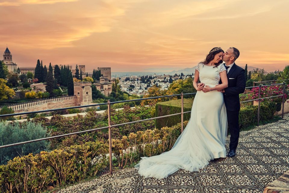 Fotografía panorámica de una pareja de novios abrazada en una terraza ajardinada.