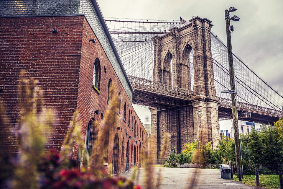 An urban photograph shows a large suspension bridge with stone towers and numerous cables.