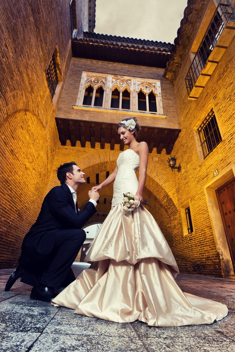 Fotografía vertical de una pareja de novios en un patio histórico de ladrillo.