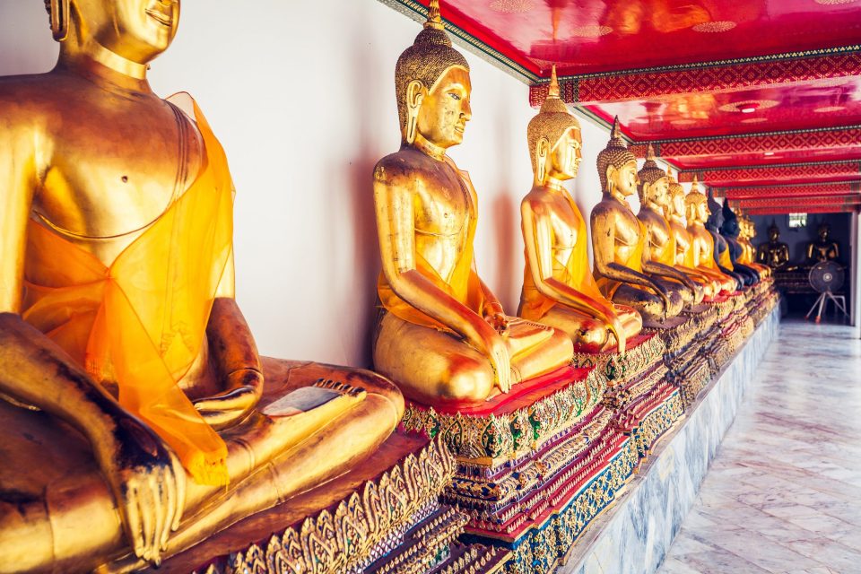 The interior of a temple with a row of seated golden Buddha statues draped in orange cloth.
