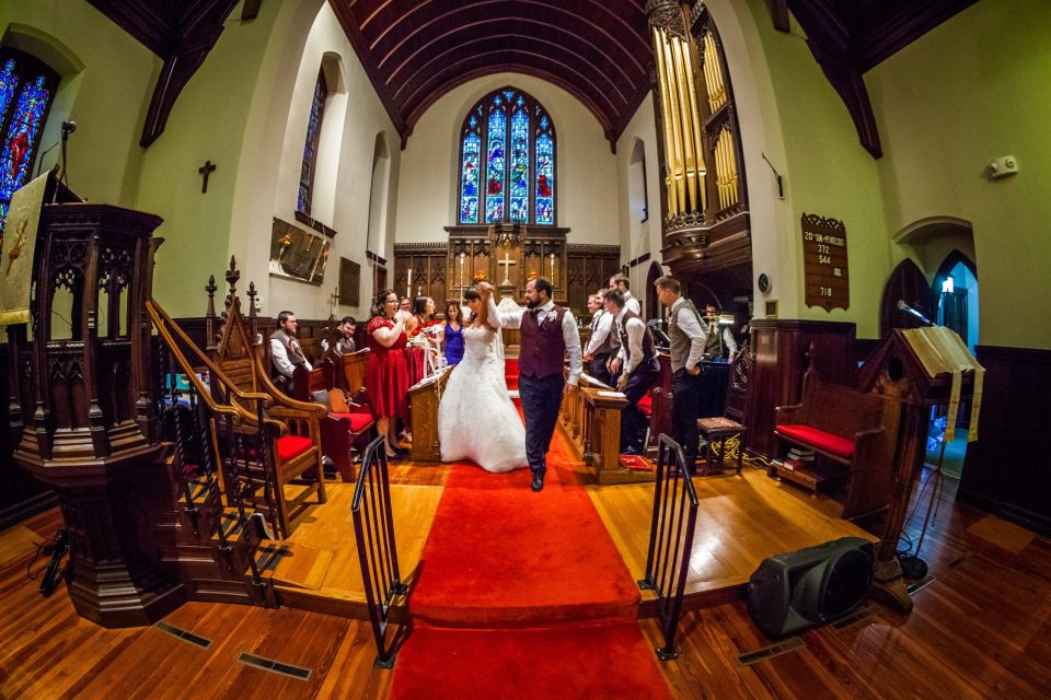 The bride and groom proceed down the central aisle of a church during the ceremony on a red carpet.