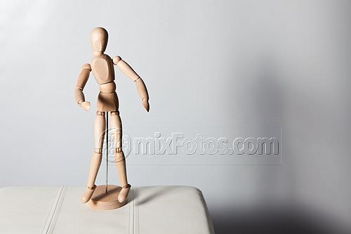 A wooden articulated mannequin is placed on a circular base on a white surface.