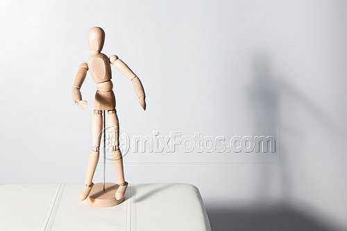 A wooden articulated mannequin is on a white surface.