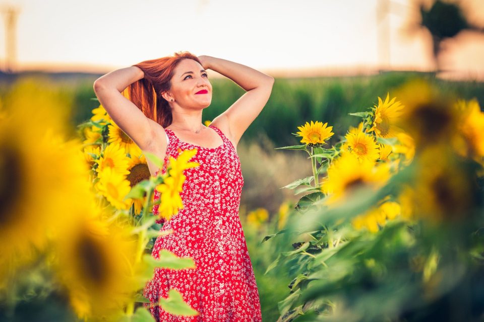 A smiling red-haired woman wears a red floral-print dress.
