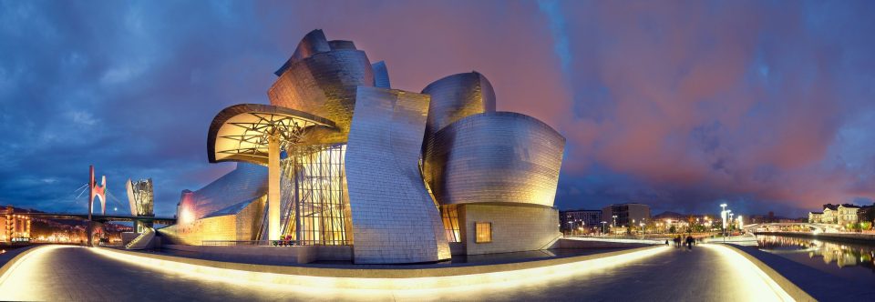 The Guggenheim Museum Bilbao is shown at night, with its curved forms and metal cladding.