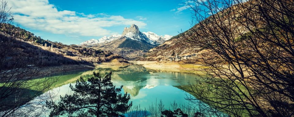 A panoramic landscape shows a turquoise-green lake surrounded by mountains.