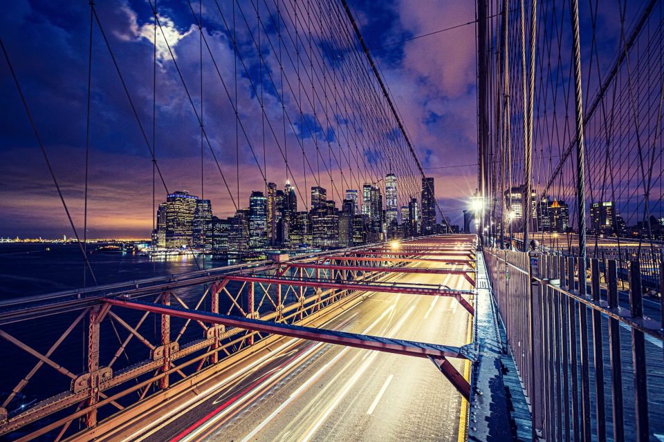 Night-time cityscape viewed from a suspension bridge.