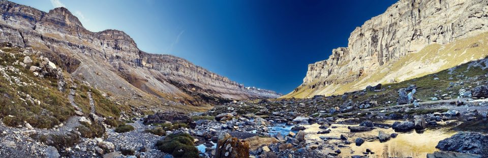 A mountain valley is surrounded by large stratified rock walls.