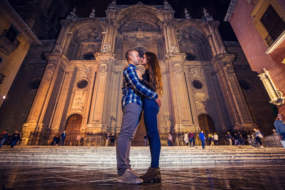 A couple embraces and kisses in front of the illuminated façade of a monumental church.