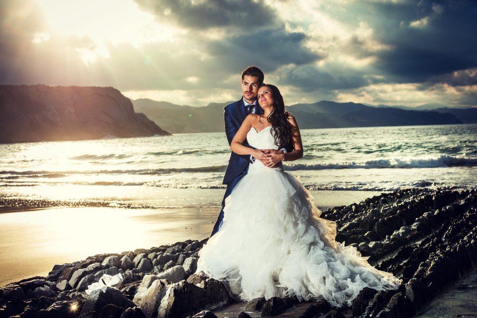 Pareja de novios abrazada sobre unas rocas junto al mar.
