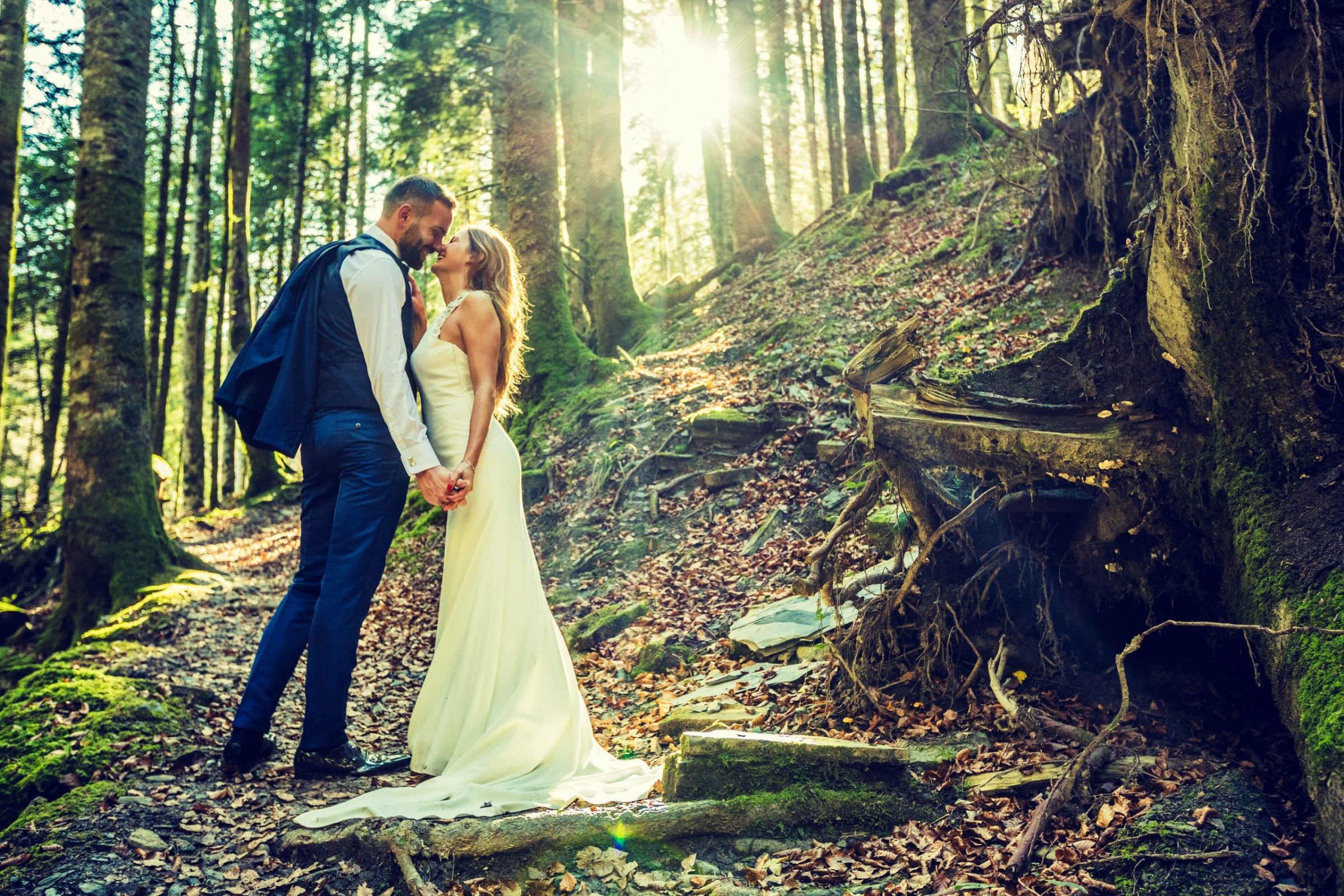 Pareja de novios besándose y sosteniéndose de la mano en un bosque de montaña.