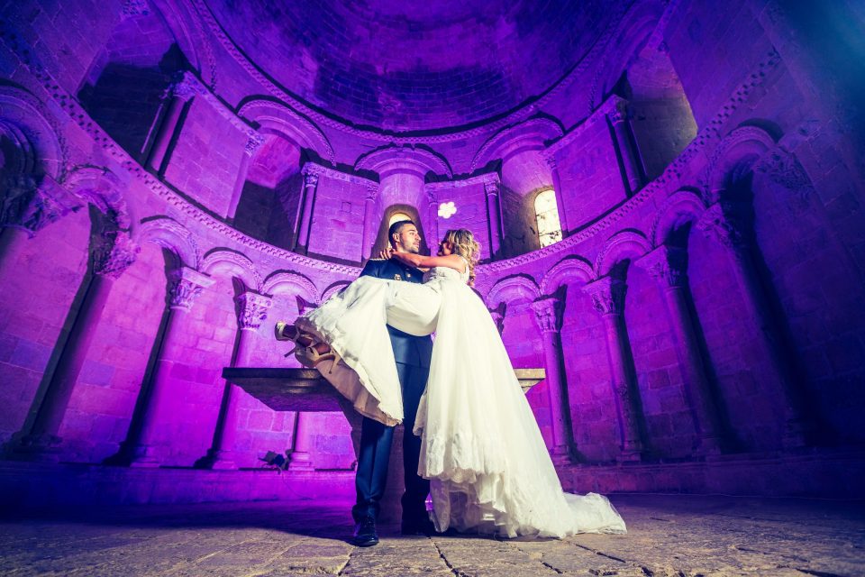 Pareja de novios en el interior de una iglesia, con el novio sosteniendo a la novia en brazos.