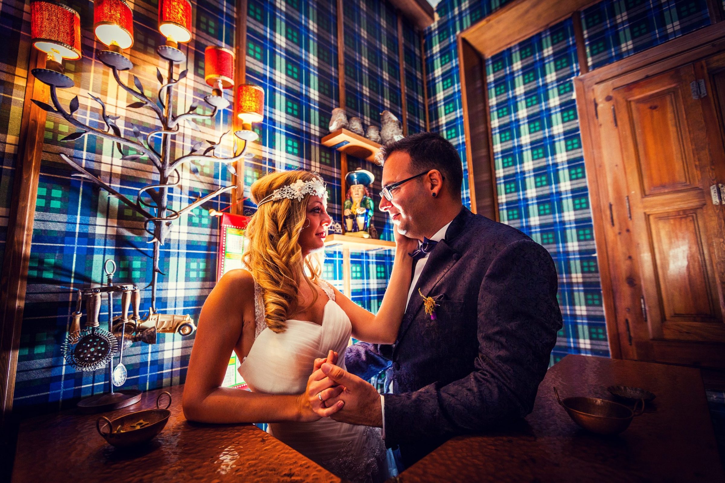 A bride and groom stand beside a wooden table in a room on an estate.
