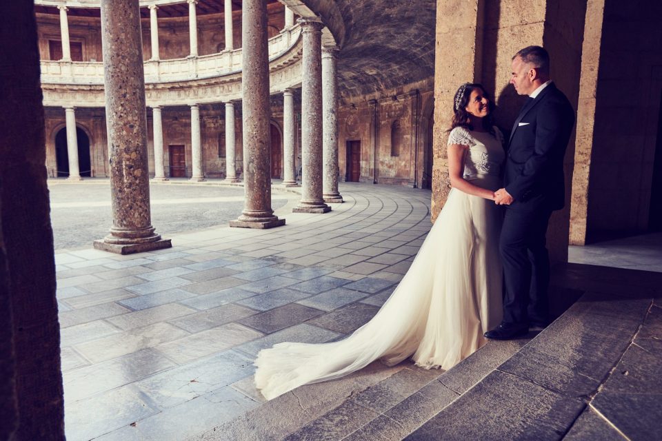 Pareja de novios posando junto a una columna de piedra en el claustro de un monumento histórico.