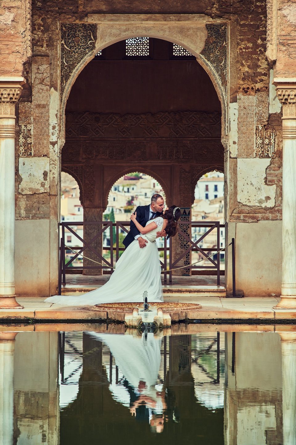 Pareja de recién casados abrazada bajo un arco ornamentado de un monumento histórico.