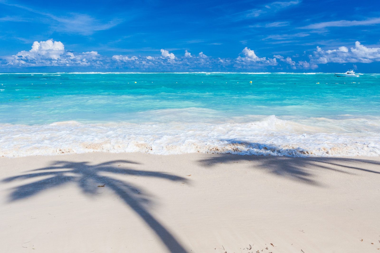 A light sandy beach beside clear turquoise waters, with small waves breaking on the shore.