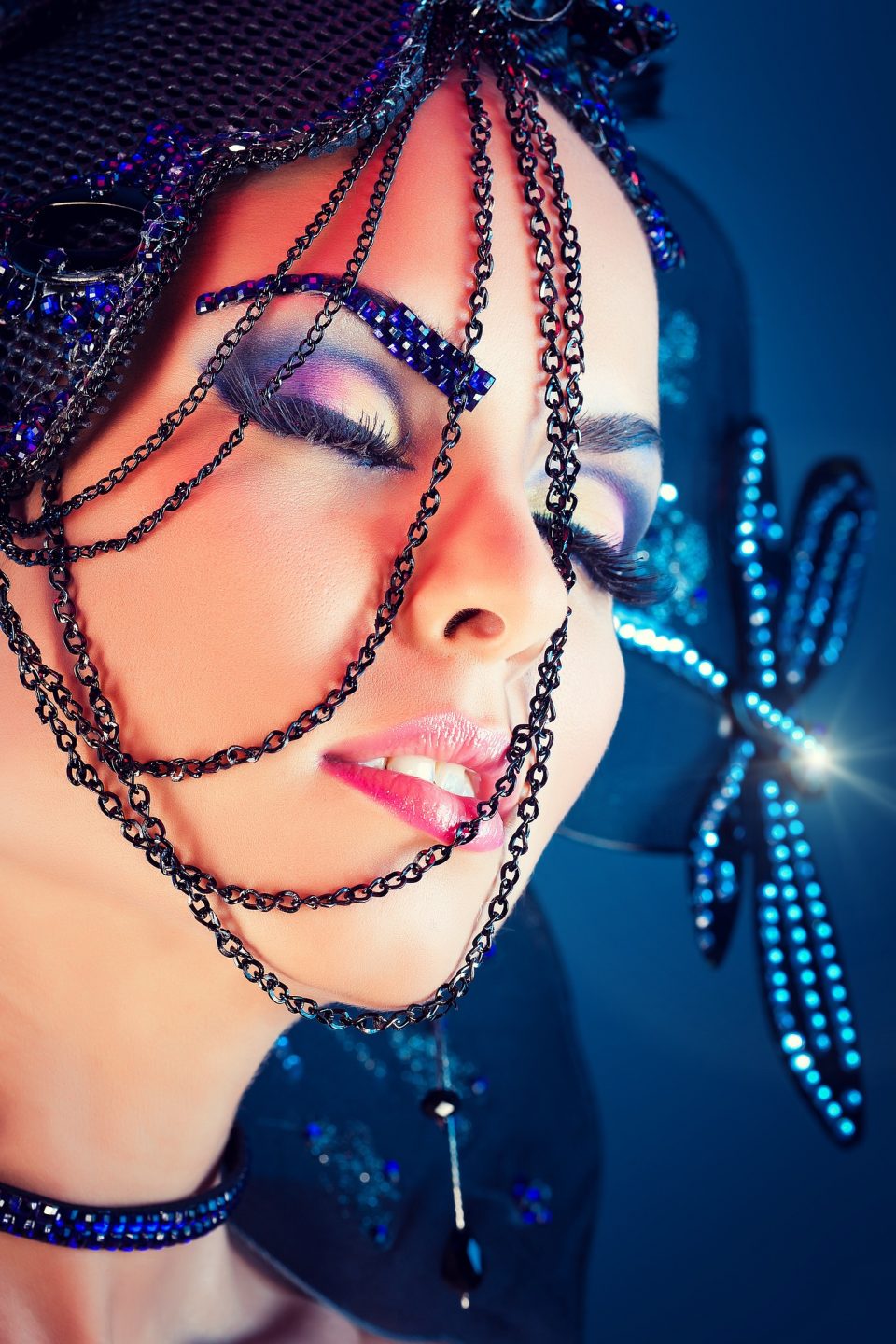 Primer plano de una modelo con los ojos cerrados, maquillaje de fantasía en tonos violeta y azul.