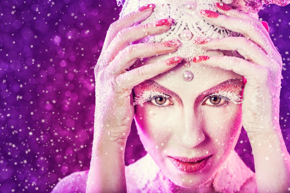 Primer plano de una modelo con maquillaje artístico de fantasía en tonos blancos, rosas y magenta.