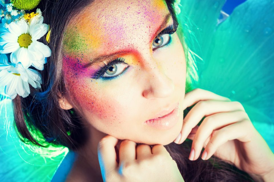 Primer plano de una modelo con maquillaje artístico multicolor y pequeñas motas de pigmento en el rostro.