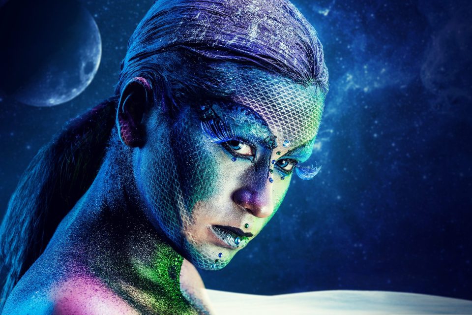 Primer plano editorial de una modelo con maquillaje artístico en tonos azul, verde y violeta.