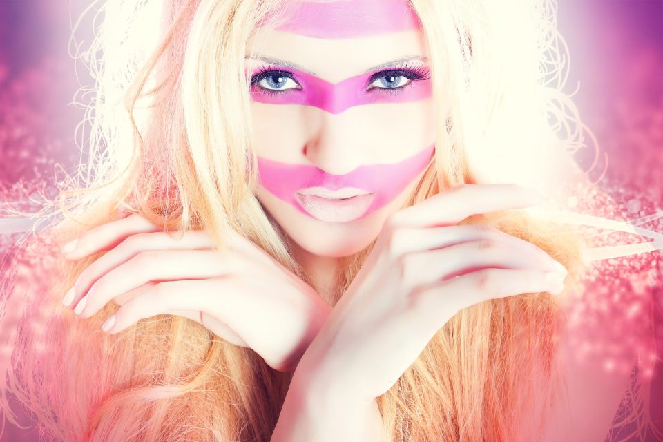Primer plano editorial de una modelo rubia con maquillaje artístico fucsia en forma geométrica alrededor de los ojos.