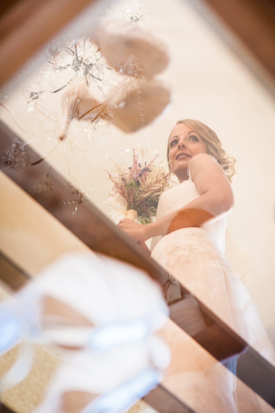 Retrato artístico de una novia con vestido blanco y ramo de flores, mirando hacia arriba en el interior de una casa.
