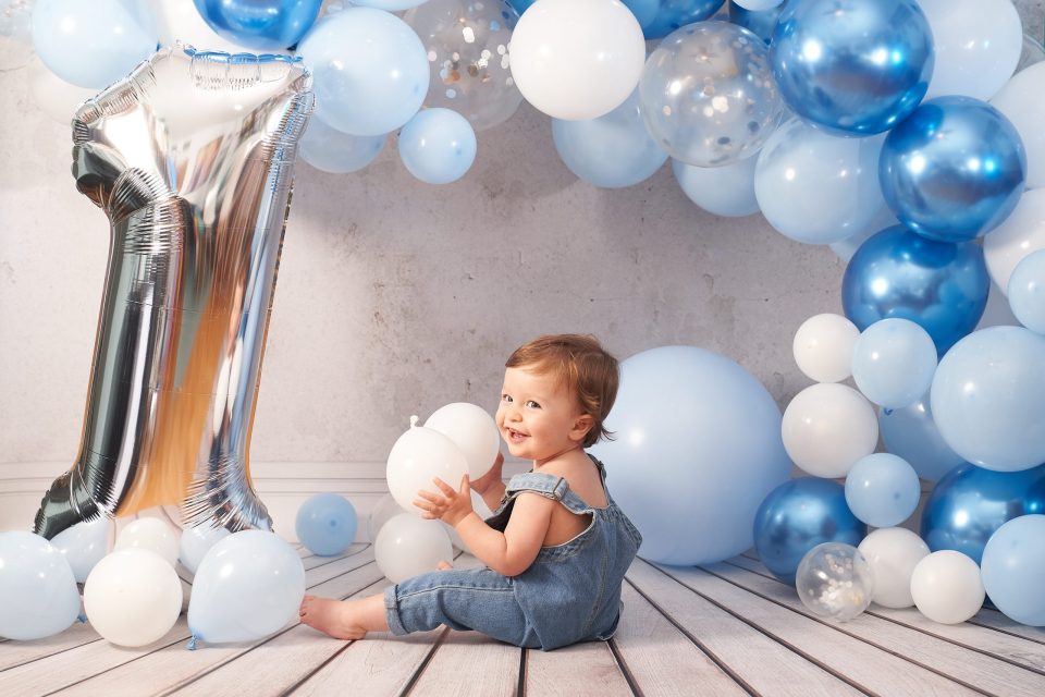 Retrato de estudio de un niño pequeño sentado en el suelo de madera y sosteniendo un globo blanco.