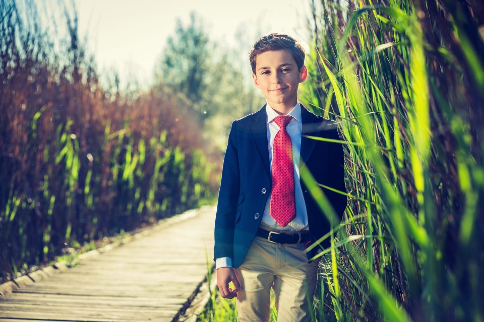 Retrato de un niño con traje azul marino, camisa blanca y corbata roja.